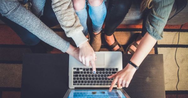 3 People sitting in front of a small silver laptop pointing at the screen