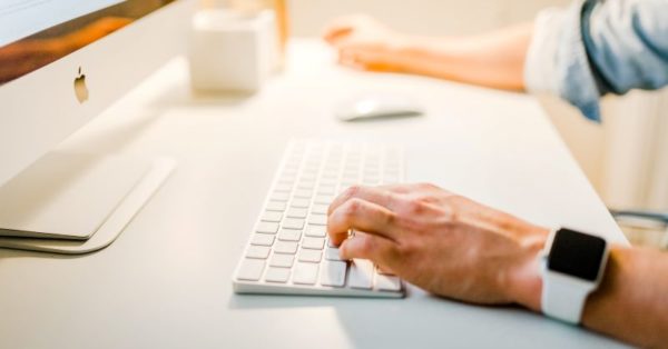 Person at an iMac wearing an Apple Watch clicking on the keyboard